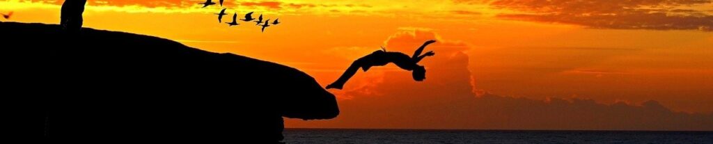 Leaping to new heights a boy does a back flip off an ocean cliff.